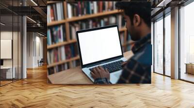 Close-up of a blank white screen on a laptop on a desk in a modern home office A young Indian man is typing with bookshelves behind him Generative AI Wall mural