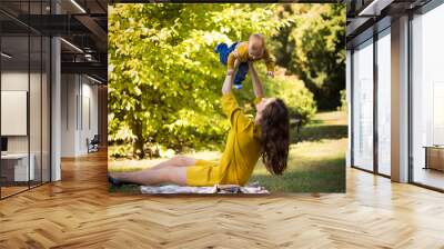 Happy young mother playing with baby in autumn park with yellow maple leaves. Family walking outdoors in autumn. Little boy with her mother playing in the park in autumn. Wall mural