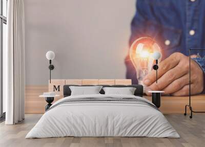 Hand holding light bulb with wooden blocks write word MARCH arranged on wooden desk with grey space wall background. Start for new idea in March concept. Wall mural