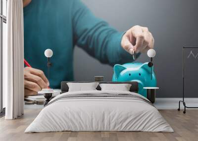 Man is dropping coins into a blue piggy bank, symbolizing the act of saving and financial responsibility. Financial planning, budgeting, and building a stable future through consistent savings Wall mural