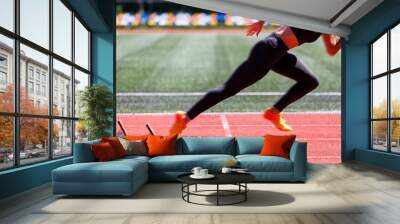 Female sprinter launches from the starting blocks with explosive power Wall mural