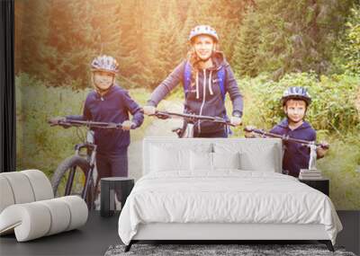 Young woman with her son and daughter enjoying cycling in forest. Family riding bike concept background Wall mural