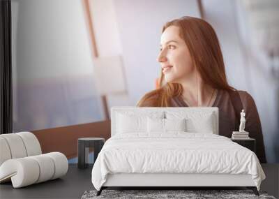 Young woman with phone standing near big window Wall mural