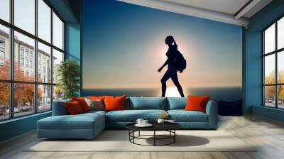 silhouette Young woman tourist with backpack goes on the background on sunset sky and sea. Wall mural