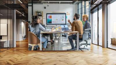 A group of people are sitting around a table in a conference room, looking at a large monitor. They are discussing a presentation on the screen. The atmosphere seems to be professional and focused Wall mural