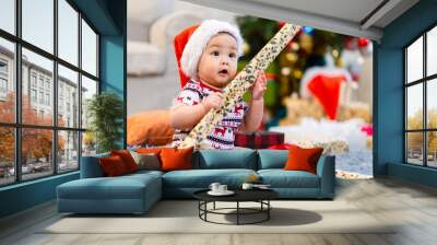 Baby in red hat on Christmas Day, filled with camera, presents and Christmas tree. Wall mural