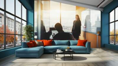 A conference meeting in a board room of a luxurious office on the top floor of a business skyscraper: a cheerful businesswoman standing near the projection screen or a whiteboard with chart and tables Wall mural