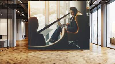 Business meeting two woman: caucasian and afro american with laptop and curly hair, both are sitting in armchairs on high floor of skyscraper near window, office luxury interior with reflections Wall mural