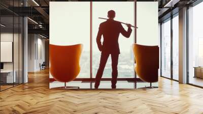 businessman in office in business suit standing between of two armchairs in front of window and hold Wall mural