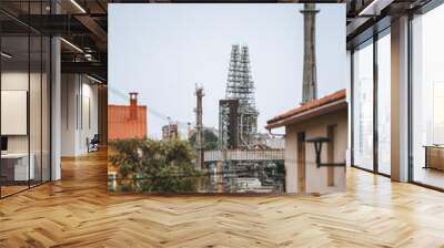 Industrial refinery complex in Coruna, Spain with tall chimneys, metal scaffolding structures, and visible residential buildings in the foreground. Clear blue sky with light clouds. Urban setting Wall mural