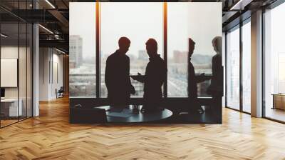 Silhouettes of two young serious successful men entrepreneurs during private meeting discussing something on screen of digital tablet in office room next to window with cityscape outside Wall mural