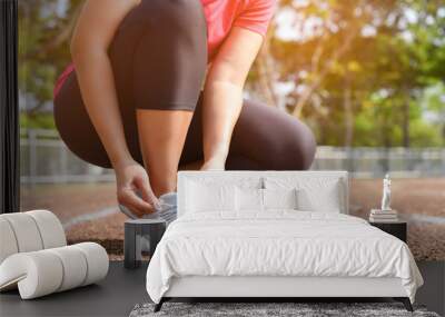 Closeup of young woman lacing running shoes for jogging outdoors on the stadium track. Fitness and healthy lifestyle concept. Wall mural