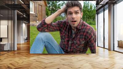 Young handsome latin man with a shock emotion chilling on the grass outside  Wall mural