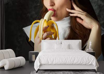 attractive nun holding a banana and bites him on a dark background Wall mural