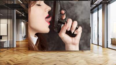 attractive nun with a gun in his hand on a dark background.close-up side view of a woman licking a gun. Wall mural