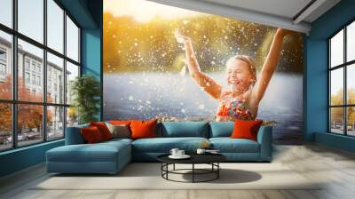 little girl playing in the river. A girl with blond hair raises her hands up in the water and splashes water drops Wall mural