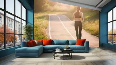 beautiful young sporty woman running on asphalt road in the Park in the morning Wall mural