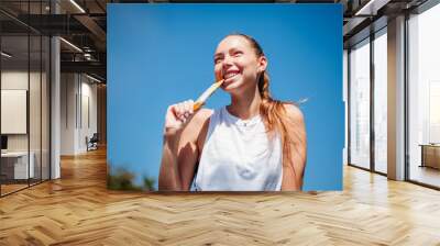 young athletic woman holding protein bar in her teeth Wall mural