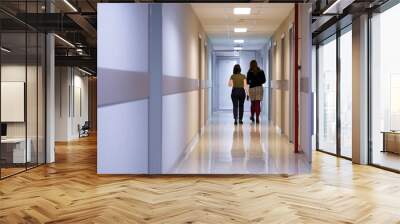 Two young women are walking along the long corridor of an office building. Work and business Wall mural