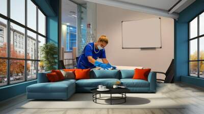 A cleaning lady with a mask on her face cleans the meeting room. Wall mural