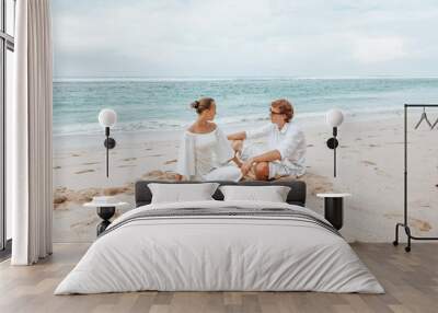 Girl and man in white clothes sitting on a white beach Wall mural