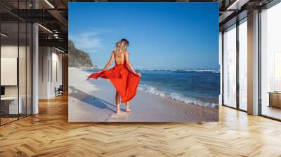 Girl walking on the beach with white sand in a red dress on the background of the ocean, the view from the back without a face. Wall mural