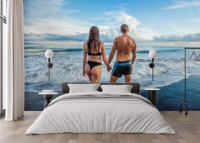 The girl and the man walk on the beach in swimsuits. Wall mural