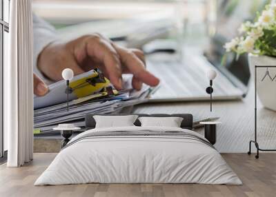 Businessman hands holding pen for working in Stacks of paper files searching information business report papers and piles of unfinished documents achieves on laptop computer desk in modern office Wall mural