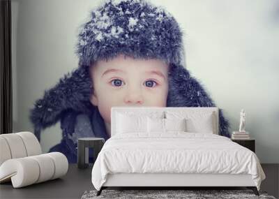 Portrait of russian cute funny little boy in cap with ear-flaps in snowy winter park during the snowfall. Image with toning and selective focus Wall mural