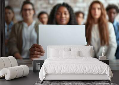 A young African American woman holds a blank sheet of paper with space for messages and text, in the background a diverse group of coworkers sitting together, unity and collaboration Wall mural