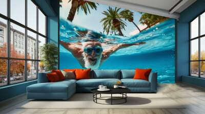 Elderly man with goggles swimming joyfully with open arms under clear blue water in a sunny resort pool.Enjoying retirement with active aging Wall mural