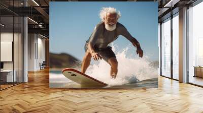 Senior with neoprene wetsuit and white beard enjoying surfing during his retirement at the beach, active aging concept. Wall mural