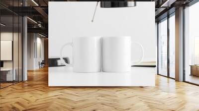 Two white mugs mockup with a lamp and a notebook on a white table. Wall mural