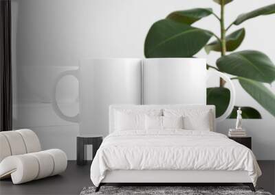 Two white mugs mockup with workspace accessories on a white table and a ficus plant. Wall mural