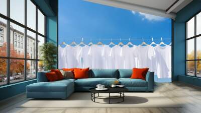 White t-shirts hanging on the line with pegs on clear blue sky background. Many simple white shirts. Wall mural