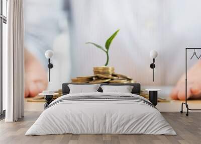 Hands of businessman putting coin into plant sprouting growing up to profit, demonstrating financial growth through saving plans and investment schemes. Wall mural