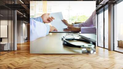 Two doctors discussing patient notes in an office pointing to a clipboard with paperwork as they make a diagnosis or decide on treatment Wall mural