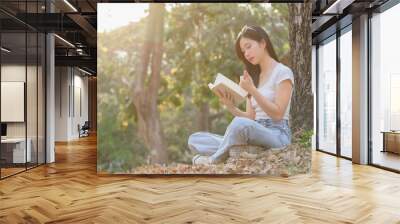 Young asian women sitting on grass under the tree to writing business data and journey dairy in notebook while enjoying and happiness to relaxation with journey travel lifestyle in the nature park Wall mural