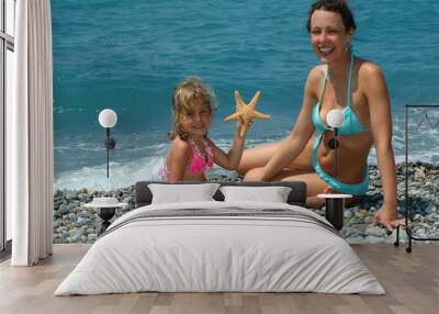 The happy young woman and child with starfish sit on a beach Wall mural