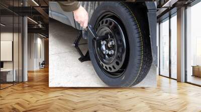 a man using an OEM  tire wrench to tighten the wheel lug nuts to install a compact spare tire of a car on a jack Wall mural