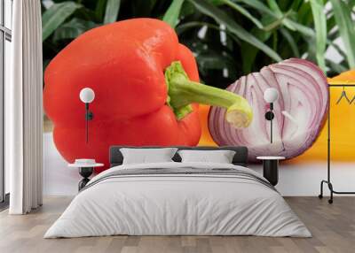 A red bell pepper with cut yellow peppers and a cut onion for salad on a white cutting board Wall mural