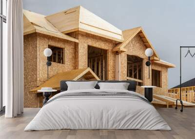 A residential frame house construction project showing the engineered truss roof rafters and oriented strand chip board engineered wall sheathing Wall mural