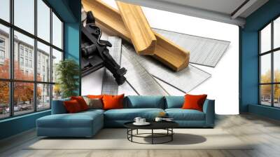 The hammer of a power nail gun with a variety of strips of finishing nails or brads in various lengths and pieces of wood trim molding isolated on white Wall mural