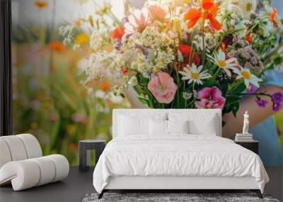 Close-up of a person holding a vibrant bouquet of wildflowers in a sunny meadow, capturing the beauty of flowers and nature. Wall mural