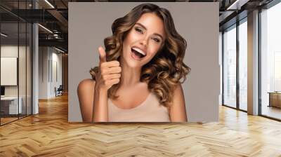 Beautiful  happy  woman with curly hair   smiling and showing thumb up positive  sign . Presenting your product. Expressive facial expressions
 Wall mural