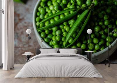 Bowl with fresh sweet peas with two open pods on the top on stone surface. Wall mural