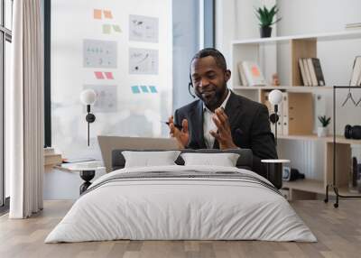 African american man in formal suit having video call at office using headset and wireless laptop. Transparent board with various graphs and charts on background. Concept of online business meeting. Wall mural