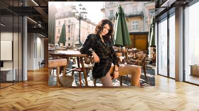 Beautiful happy smiling girl with dark hair, nude makeup, wearing stylish black jacket posing in street cafe. Outdoor portrait, day light. Female autumn fashion concept. Copy, empty space for text Wall mural