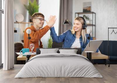 Cheerful young couple of friends, boy and girl, giving high five each other while celebrating success after playing game. Happy people using joystick for new video game, spending time at home Wall mural