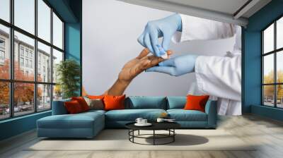 Close up cropped photo of hands of a female lab worker in white coat and gloves, taking a patient's blood sample, using painless scarifier. Black woman patient ready to blood test Wall mural